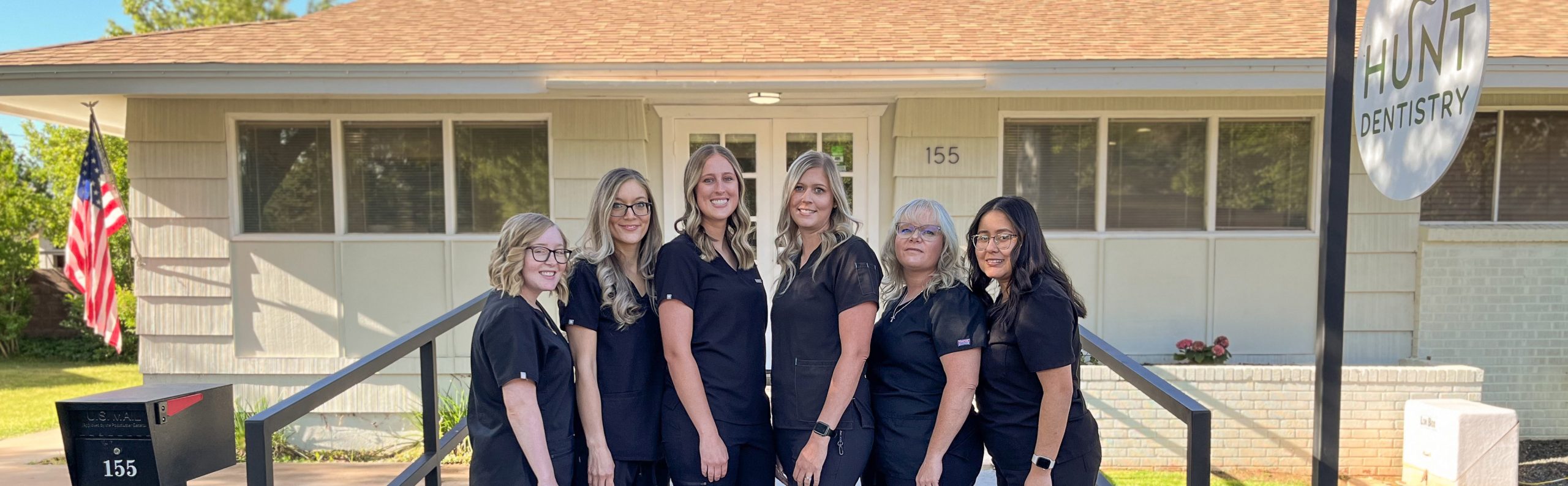 Team of six smiling woman outside of a dental office on a sunny day