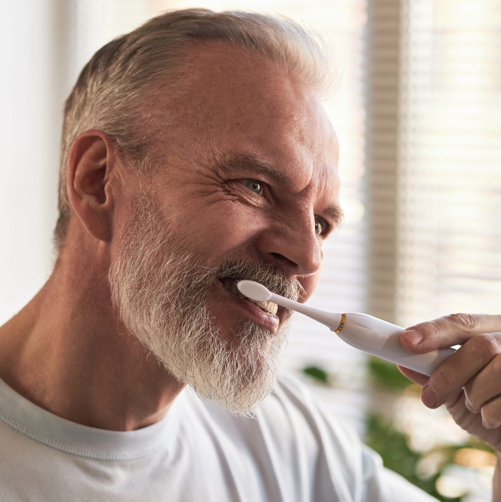 Middle Aged Caucasian Man Brushing Teeth with Electric Toothbrush Indoors